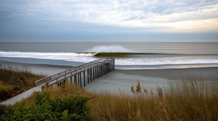 Obraz premium Pier is seen in front of the ocean, with a wave crashing in the background. The sky is cloudy, giving the scene a somewhat somber mood