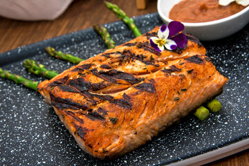 Grilled salmon garnished with asparagus, sauces and dressings on restaurant table, decorated with flowers	