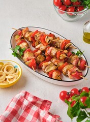 Step-by-step preparation of skewers on a skewer made of chicken, sweet pepper, bacon and onion on a light concrete background.