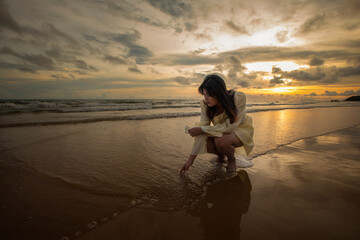Beautiful Asian woman walking peacefully on a desert beach during sunset, with freedom concept, with amazing orange sky and sunlight reflecting on the sea and sand.