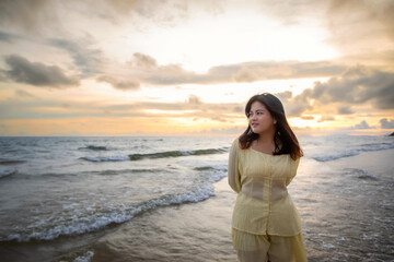Beautiful Asian woman walking peacefully on a desert beach during sunset, with freedom concept, with amazing orange sky and sunlight reflecting on the sea and sand.