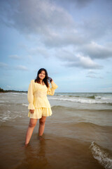 Beautiful Asian woman walking peacefully on a desert beach during sunset, with freedom concept, with amazing orange sky and sunlight reflecting on the sea and sand.