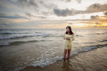 Beautiful Asian woman walking peacefully on a desert beach during sunset, with freedom concept, with amazing orange sky and sunlight reflecting on the sea and sand.