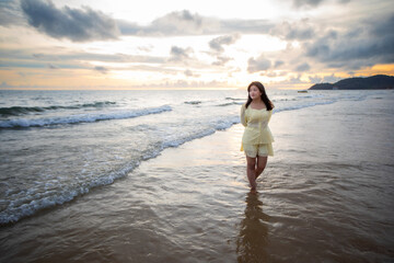 Beautiful Asian woman walking peacefully on a desert beach during sunset, with freedom concept, with amazing orange sky and sunlight reflecting on the sea and sand.