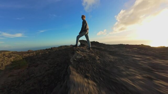 Aerial view capturing volcanic terrain during sunset, revealing hardened lava flows with solitary hiker overlooking dramatic rocky landscape