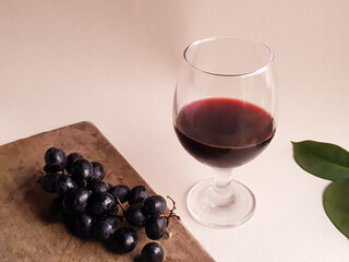 red wine in glass cup with grapes light background