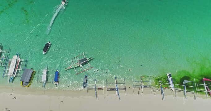 Aerial view of White Beach in Boracay, Philippines, featuring iconic paraw sailboats in turquoise waters, with a speedboat enhancing the vibrant tropical scene