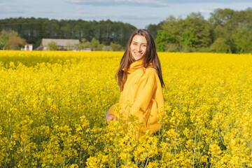 Young beautiful woman in a yellow hoodie close up in the middle of the yellow field with rapeseed...