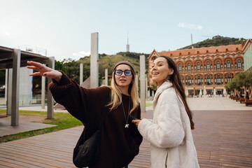 A woman stands and smiles while looking in the direction pointed by a female friend who is standing...