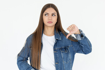 Young sad displeased unhappy woman wear white t-shirt and jeans coat showing thumb down dislike...