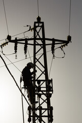Al atardecer, figura de un Técnico de compañía eléctrica subido en un poste dañado para cambiar transformador de alta tensión, reparación de cableado eléctrico, Apagón 