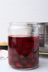 Tasty cherry compot in glass jar on white tiled table, closeup