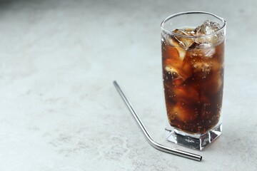 Refreshing cola with ice cubes in glass and straw on grey textured table, closeup. Space for text