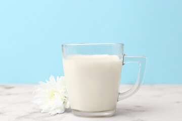 Cup of milk and flower on white marble table against light blue background