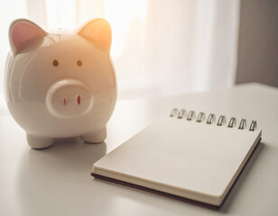A white piggy bank is positioned adjacent to a notebook on a white table.
