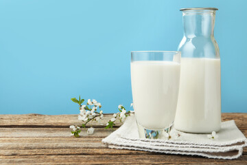 Fresh milk and blossoms on wooden table against light blue background, closeup. Space for text