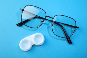 Contact lenses in case and glasses on blue background, flat lay