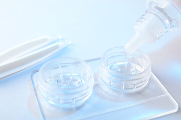 Dripping solution into case with contact lenses on light background, closeup