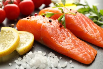 Seafood. Pieces of salmon fillet, spices, lemon slices and tomatoes on gray table, closeup