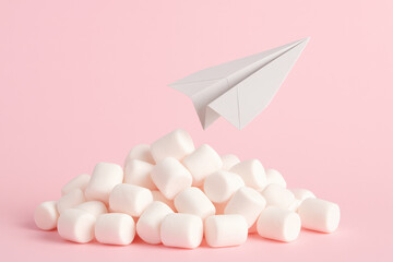Paper airplane flying over marshmallows on pink background