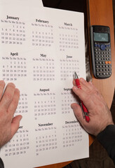 Hands planning schedule with printed calendar and calculator
