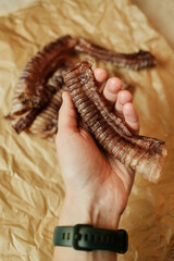 A hand holding a natural dried beef trachea - a healthy chew treat for dogs. Close-up shot highlighting the texture and quality of the single-ingredient pet snack on craft paper.