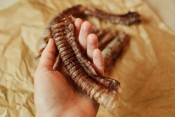 A hand holding a natural dried beef trachea - a healthy chew treat for dogs. Close-up shot highlighting the texture and quality of the single-ingredient pet snack on craft paper.