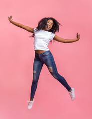 Carefree attractive black girl jumping in the air, pretending she is flying, pink background