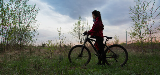Young woman riding a bicycle on the spring field with green grass on sunset sky landscape...