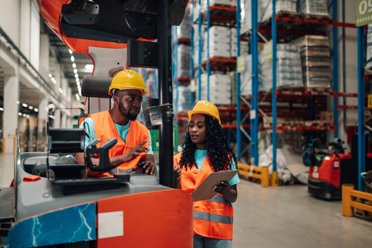 Warehouse workers discussing logistics using forklift and clipboard
