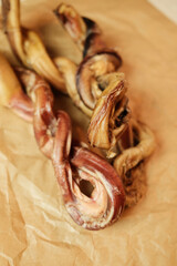 Natural dried bull pizzle dog chews, twisted and displayed on kraft paper. High-protein, long-lasting treats for dogs. Single-ingredient, air-dried product for healthy pet chewing.