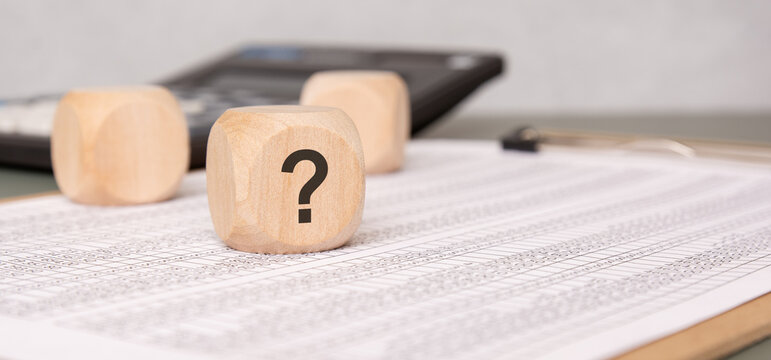 Wooden block with question mark on financial document, symbolizing uncertainty
