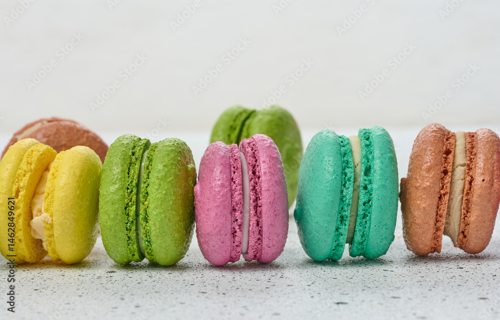 Poster an assortment of colorful macarons on a white surface with dark speckles. the macarons have a smooth