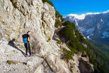 Young woman with backpack hiking along the path in the scenic Julian Alps, Italy, Europe