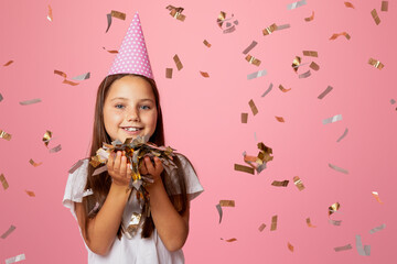 Children party. Happy little kid girl in cap, holds confetti, isolated on pink background, studio...