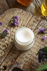 A glass jar of homemade comfrey root ointment with fresh blooming plant