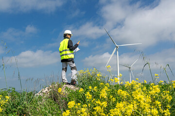Female engineer inspecting wind turbines in a blooming field