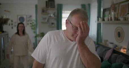 Obraz premium Couple in heated argument in living room, man standing visibly upset, woman gesturing emotionally in background, tense moment during relationship conflict