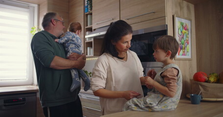 Family interaction in modern kitchen, mother comforting child sitting on countertop while father...