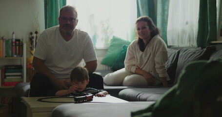 Father and mother sitting on couch smiling at child playing with toy train on coffee table in cozy living room setting, joyful family moment, indoor bonding time