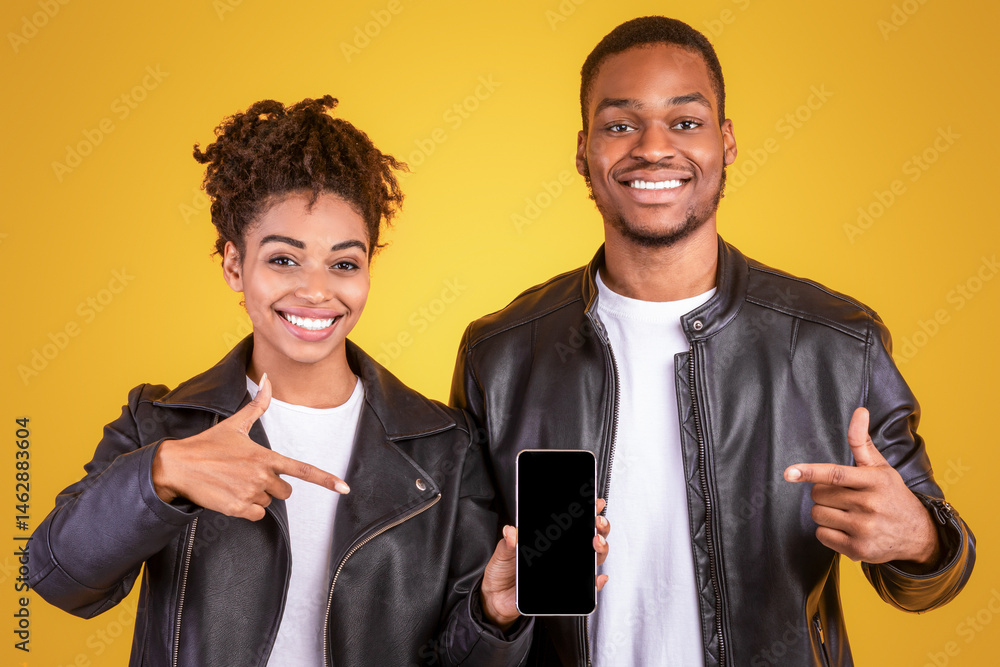 Poster cheerful black couple showing smartphone with blank screen pointing fingers recommending mobile app 
