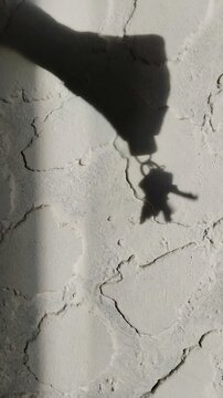 Un primer plano de una sombra de una mano de mujer moviendo unas llaves en una pared de fondo blanco. Video vertical