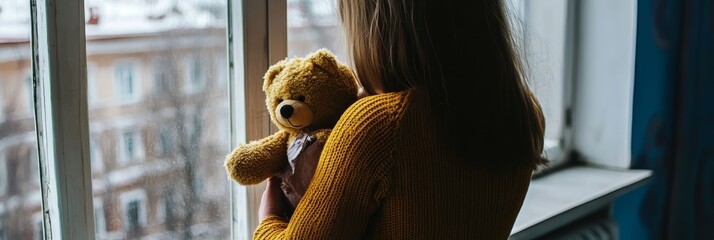 The little girl holds a bear in her arms, she is sad. The theme of domestic violence and violence against children.