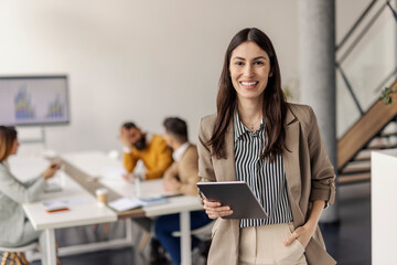 Portrait of smiling successful businesswoman with tablet standing at corporate firm in boardroom...