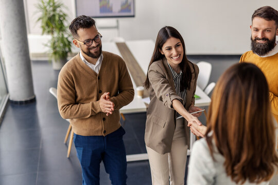 Group of businesspeople standing at corporate office and shaking hands with businesswoman, welcoming her into team of experts.