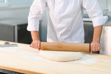 While working in bakery using rolling pin, male cook makes thin flat cakes from dough with rolling pin