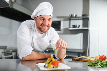 food cooking, profession and people concept - happy male chef cook with plate of salad at restaurant kitchen table