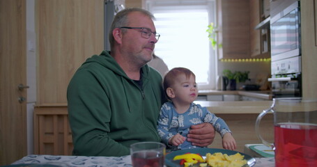 Father holding baby during family meal, baby gazing upwards with curiosity while sitting at dining...