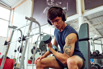 Young athlete lifting weights and listening to music in gym