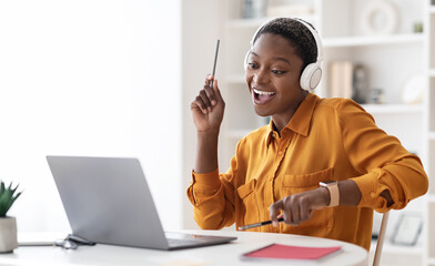 Joyful short-haired millennial black lady having break while working at office, watching video on...